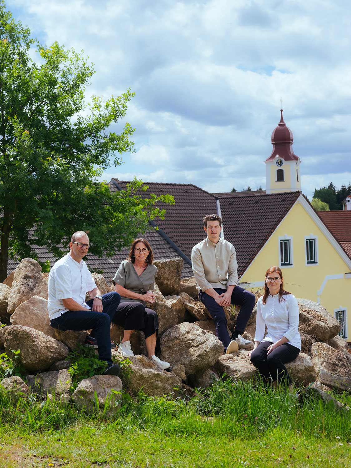 Mehrere Personen sitzen auf großen Steinen, im Hintergrund sind Häuser und der Kirchturm